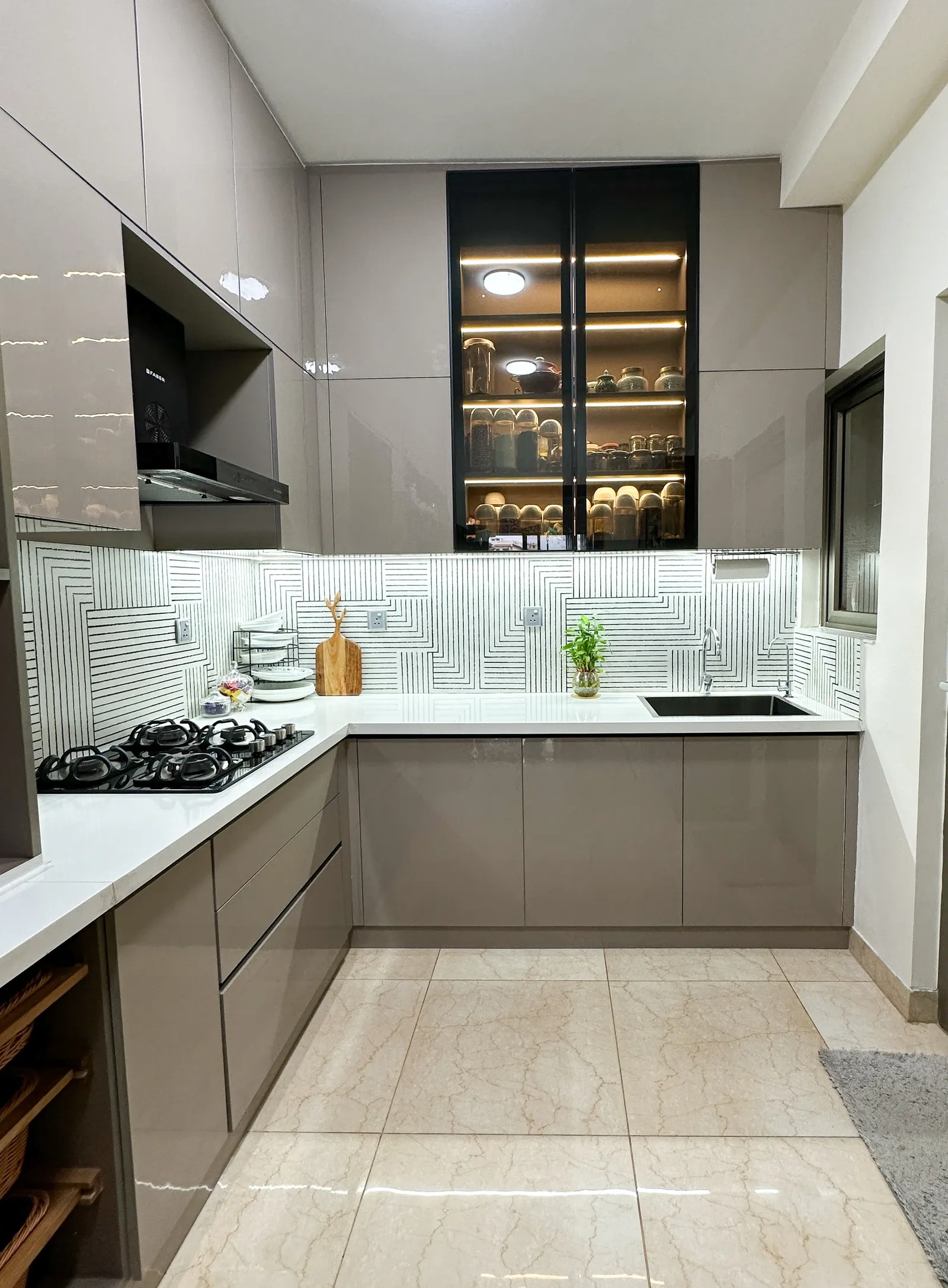 Modular kitchen with lit glass crockery unit and white countertop — Somani's Residence